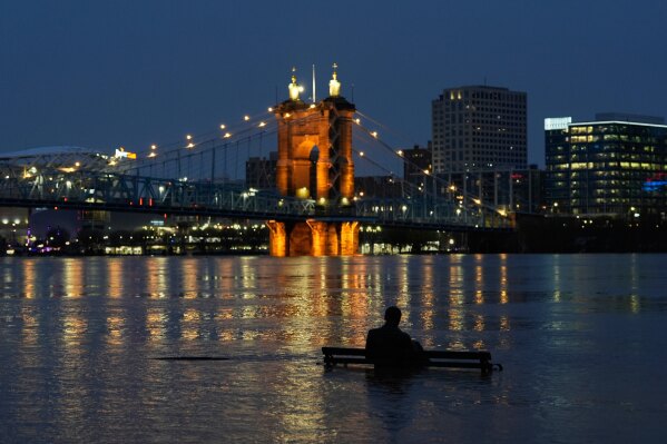 The rising Ohio River partially submerges the bronze statue of James Bradley along Riverside Drive, Sunday, April 6, 2025, in Covington, Ky. Cincinnati and the John A. Roebling Suspension Bridge are seen across the Ohio River. (AP Photo/Carolyn Kaster)