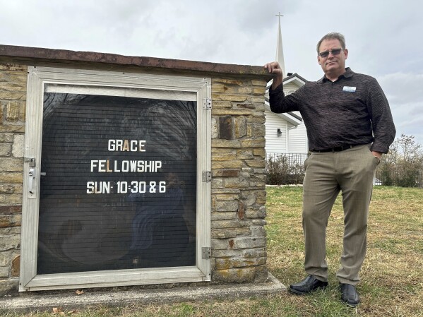 Pastor Kenny Batson stands near a sign displaying the worship service times of Grace Fellowship Church on Nov. 16, 2023, in El Dorado Springs, Mo. Batson was convicted of a series of crimes in the 1990s but became a Christian pastor after being released from prison. He was pardoned by Missouri Gov. Mike Parson. (AP Photo/David A.Lieb)