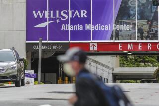 FILEE - A masked man passes Wellstar Atlanta Medical Center on Boulevard in Atlanta on May 20, 2020. WellStar announced late Wednesday, Aug. 31, 2022, that the Atlanta Medical Center will close in two months after experiencing more than $100 million in losses over the past year. (John Spink/Atlanta Journal-Constitution via AP, File)