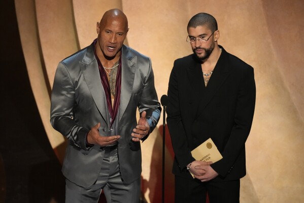 Dwayne Johnson, left, and Bad Bunny present the award for best international feature film during the Oscars on Sunday, March 10, 2024, at the Dolby Theatre in Los Angeles. (AP Photo/Chris Pizzello)