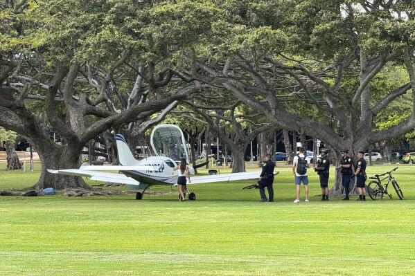 Police officers stand near a small plane that landed in Kapiolani Park in Honolulu on Tuesday, April 16, 2024. Officials say no one was injured when the plane lost power and landed safely in the sprawling park near the tourist mecca of Waikiki. (Millie Dydasco via AP)