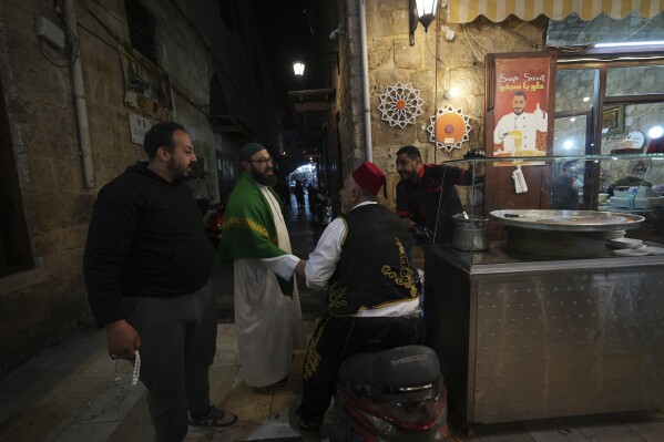 Mahmoud Fanas, second left, a "musaharati,"or "dawn caller," who beats on a drum to wake up Muslims for a meal before sunrise during Ramadan, speaks with friends as walks through old streets in the southern Lebanese port city of Sidon, Lebanon, Sunday, March 16, 2025. (AP Photo/Hassan Ammar)