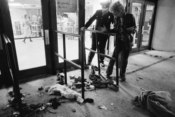 FILE - A security guard and an unidentified man look at an area with shows and clothes strewn around where several people were killed and others injured, as they were caught in a surging crowd entering Cincinnati's Riverfront Coliseum for a Who concert on Dec. 3, 1979. The crowd deaths at a Houston music festival on Friday, Nov. 5, 2021, have added to the long list of people who have been crushed at a major event. Such tragedies have been occurring around the world for a long time at concerts, sports events and religious gatherings. (AP Photo/Brian Horton, File)