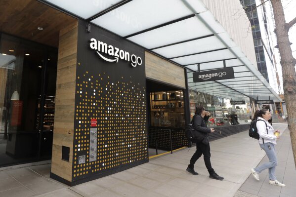 FILE - In this March 4, 2020 file photo, people walk out of an Amazon Go store, in Seattle. Amazon is rolling out a new device for contactless transactions that will scan an individual’s palm. The Amazon One, which will initially launch in two Amazon Go stores in Seattle, is being viewed as a way for people to use their palm to make everyday activities like paying at a store easier. (AP Photo/Ted S. Warren, File)