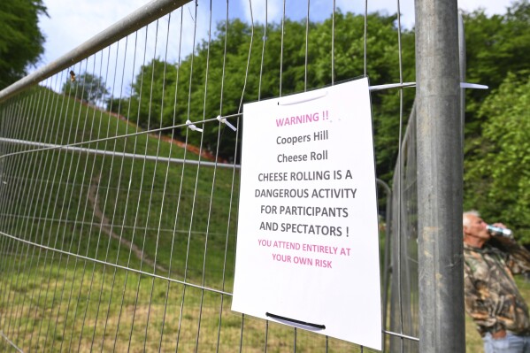 A signpost warns participants and spectators of the dangers of the traditional annual Cheese Rolling contest at Cooper's Hill in Brockworth, Gloucestershire, England, Monday, May 26, 2025.(AP Photo/Anthony Upton)