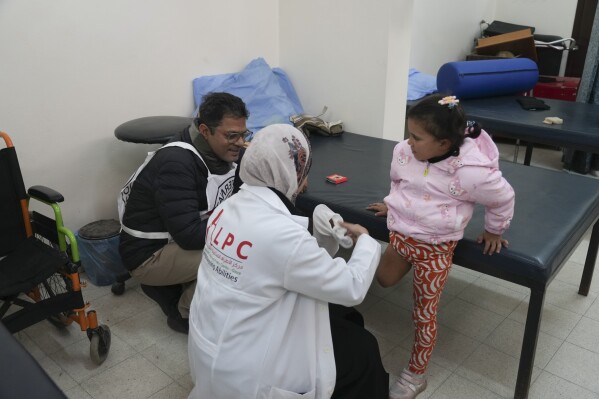 Doctors assist Five-year-old Palestinian Sila Abu Aqlan to put on her new prosthetic leg at the Artificial Limbs and Polio Center in Gaza City, on Tuesday, Feb. 18, 2025, (AP Photo/Abdel Kareem Hana)