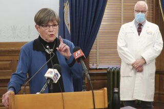 Kansas Gov. Laura Kelly discusses the coronavirus pandemic as her health secretary, Dr. Lee Norman, watches behind her at a news conference, Tuesday, Nov. 10, 2020, at the Statehouse in Topeka, Kan. Kelly says the state's unified strategy for more aggressive testing won't work to curb the spread of the virus if people don't wear face masks and socially distance. (AP Photo/John Hanna)
