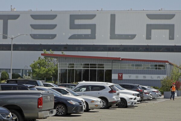FILE - A man walks in the Tesla plant parking lot, May 11, 2020, in Fremont, Calif. Factory workers at Tesla have been told to expect pay raises in 2024, a move that comes as the United Auto Workers union tries to organize the electric vehicle maker's U.S. plants. The UAW said Thursday, Jan. 11, 2024, that Tesla workers have told the union about company statements on the raises, which did not give details about the size of the increases. (AP Photo/Ben Margot, File)