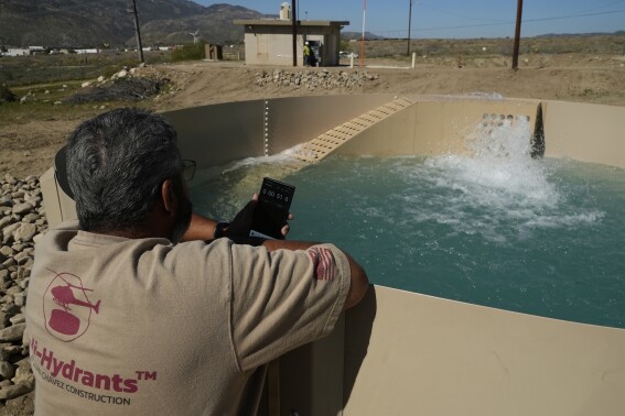 Glenn Chavez sets a timer as water fills a newly installed Heli-Hydrant, a small, open tank that helicopters can rely on to get water faster for urban fires, Friday, April 11, 2025, in Cabazon, Calif. (AP Photo/Brittany Peterson)