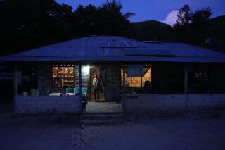 Bara Kilimandang stands at the door of his house whose electricity comes from solar energy in Walatungga on Sumba Island, Indonesia, Tuesday, March 21, 2023. In Indonesia's far-east island, off-grid solar is lighting up lives for residents still living out of reach of the country's national electricity provider. (AP Photo/Dita Alangkara)