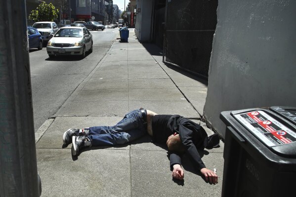 FILE - In this April 26, 2018, file photo, a man lies on the sidewalk beside a recyclable trash bin in San Francisco. San Francisco supervisors consider legislation Tuesday, June 4, 2019, allowing the city to force mentally ill drug addicts into housing and treatment for up to a year. Mayor London Breed says it's inhumane to let addicts languish on the streets, but homeless advocates say the measure is extreme and a violation of civil rights. (AP Photo/Ben Margot, File)