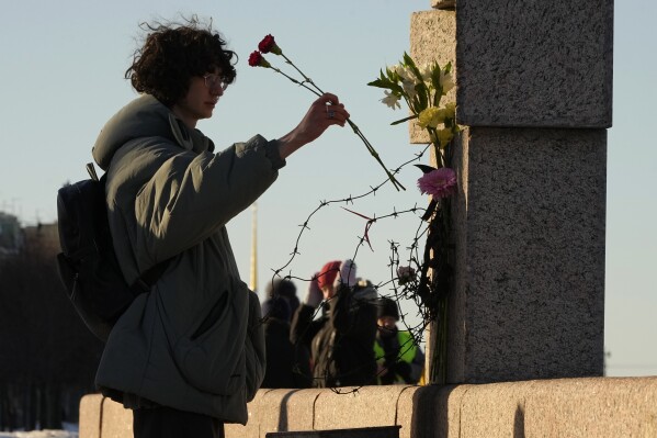 A woman places flowers as people pay tribute to Alexei Navalny at the Memorial to Victims of Political Repression in St. Petersburg, Russia, Sunday, Feb. 18, 2024. Russians across the vast country streamed to ad-hoc memorials with flowers and candles to pay tribute to Alexei Navalny, the most famous Russian opposition leader and the Kremlin's fiercest critic. Russian officials reported that Navalny, 47, died in prison on Friday. (AP Photo/Dmitri Lovetsky)