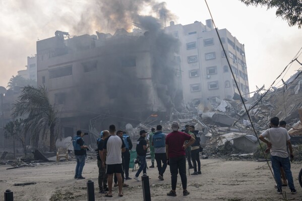 FILE - Journalists observe as Palestinians inspect the rubble of a building after it was struck by an Israeli airstrike, in Gaza City, Sunday, Oct. 8, 2023. Journalists reporting in Gaza need to worry about basic survival for themselves and their families in addition to getting out the story of a besieged population. (AP Photo/Fatima Shbair, File)