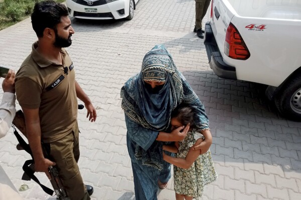 Police officers escort a relative and a child of a couple wanted by British police in connection with last month's death of the couple's young daughter on the outskirts of London, to appear in a court in Jhelum, Pakistan, about 175 kilometres (110 miles) northwest of Lahore, Tuesday, Sept. 12, 2023. Sara Sharif, 10, was found dead at her British home on Aug. 10. A Pakistani court ordered her five siblings put in the custody of a children's protection center. The police are continuing their search for the girl’s father and stepmother. (AP Photo/Tahir Mahmood)