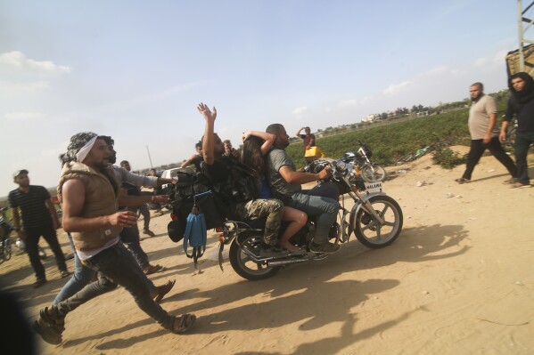 Palestinians transport a captured Israeli civilian, center, from Kfar Azza kibbutz into the Gaza Strip on Saturday, Oct. 7, 2023. The militant Hamas rulers of the Gaza Strip carried out an unprecedented, multi-front attack on Israel at daybreak Saturday, firing thousands of rockets as dozens of Hamas fighters infiltrated the heavily fortified border in several locations by air, land, and sea and catching the country off-guard on a major holiday. (AP Photo)