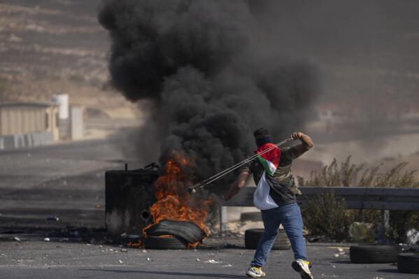 A Palestinian protester uses a slingshot during clashes with Israeli army troops in the West Bank city of Ramallah, Thursday, Oct. 20, 2022. Palestinians launched a general strike on Thursday throughout the West Bank and east Jerusalem in response to the death of a suspected Palestinian attacker. (AP Photo/Nasser Nasser)