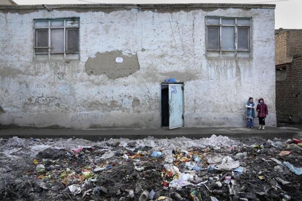 Two young girls stand outside their house on a garbage strewn street, in Kabul, Afghanistan, Feb. 8, 2022. (AP Photo/Hussein Malla)