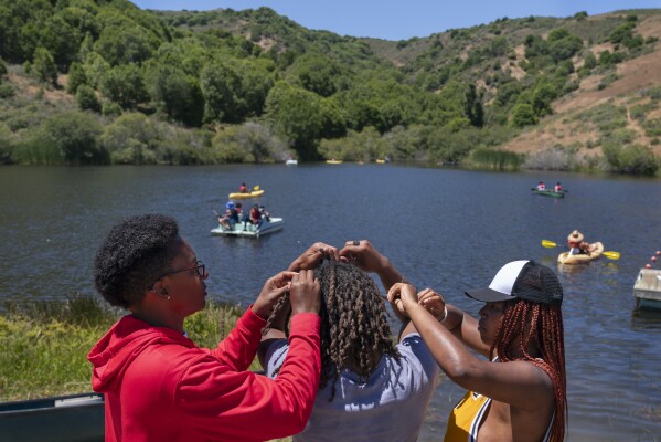 Camp sports director Cellie Davis, 39, left, of Houston, and counselor Satya Sheftel-Gomes, 22, of San Francisco, right, undo the two-strand-twists from the locs in the hair of 17-year-old junior counselor Jordan Gardner, of Novato, Calif., as campers enjoy the lake at Camp Be’chol Lashon, a sleepaway camp for Jewish children of color, Friday, July 28, 2023, in Petaluma, Calif., at Walker Creek Ranch. (AP Photo/Jacquelyn Martin)
