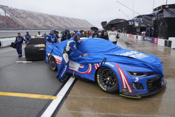 Crews push covered cars to the garage after a NASCAR Cup Series auto race was postponed for rain at Michigan International Speedway in Brooklyn, Mich., Sunday, Aug. 6, 2023. (AP Photo/Paul Sancya)