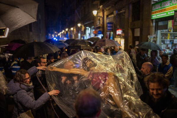 Worshippers cover the image of the Holy Christ of the Blood with a plastic sheet while it rains, during a procession asking for rain through the streets of downtown Barcelona, Spain, Saturday, March 9, 2024. Preceded by nine days of prayers and emulating a documented historical tradition dating back five hundred years, worshippers requested rain as Catalonia last month declared drought emergency for the area of around 6 million people including the city of Barcelona. (AP Photo/Emilio Morenatti)