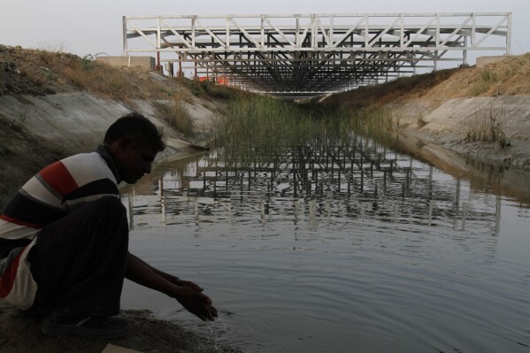 FILE - A worker washes his hands as installed solar panels are visible atop the Narmada canal at Chandrasan village, outside of Ahmadabad, India, Feb. 16, 2012. The project brings water to hundreds of thousands of villages in the dry, arid regions of western India’s Gujarat state. (AP Photo/Ajit Solanki, File)