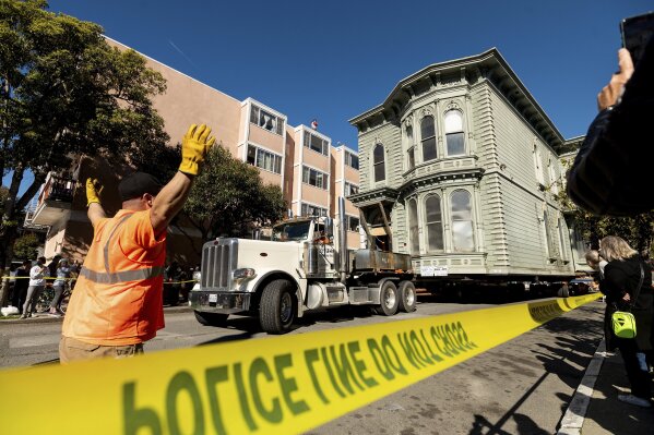 CORRECTS APPROXIMATE COST TO $400,000, INTEAD OF $200,000 - A worker signals to a truck driver pulling a Victorian home through San Francisco on Sunday, Feb. 21, 2021. The house, built in 1882, was moved to a new location about six blocks away to make room for a condominium development. According to the consultant overseeing the project, the move cost approximately $400,000 and involved removing street lights, parking meters, and utility lines. (AP Photo/Noah Berger)