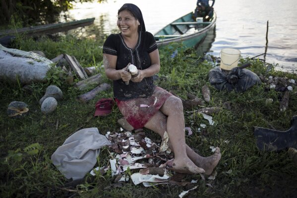 Andrea Rodrigo, a member of the Israelites of the New Universal Pact religious group, removes the husk from a yucca or cassava root, on the banks of the Amazon River in Jose Carlos Mariategui, Peru, Wednesday, March 31, 2021. The 21-year-old Peruvian woman makes yucca flour that her family sells in markets along Peru's remote borders with Brazil and Colombia. (AP Photo/Rodrigo Abd)