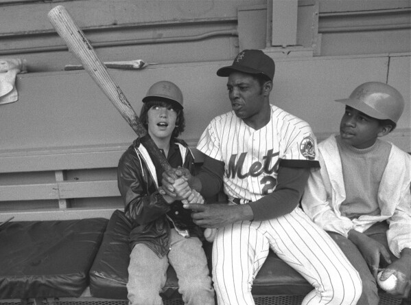 FILE - New York Mets' Willie Mays, center, shows John F. Kennedy Jr., left, the proper grip on the bat June 3, 1972, in the dugout at New York's Shea Stadium. At right is Eric Von Huguley, a friend who joined young John in a visit to the Mets' dugout before the game against the Atlanta Braves. Mays, the electrifying “Say Hey Kid” whose singular combination of talent, drive and exuberance made him one of baseball’s greatest and most beloved players, has died. He was 93. Mays' family and the San Francisco Giants jointly announced Tuesday night, June 18, 2024, he had “passed away peacefully” Tuesday afternoon surrounded by loved ones. (AP Photo, File)