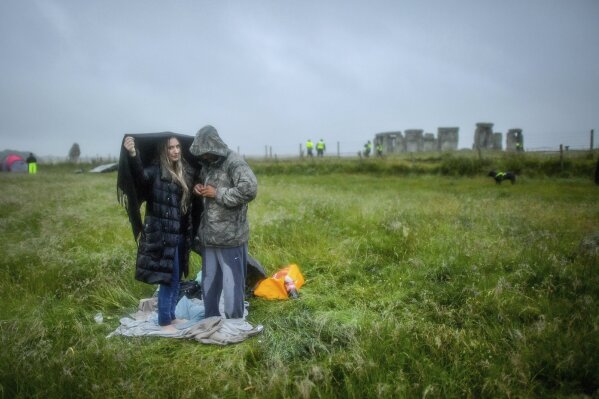 People shield from the rain next to the closed Stonehenge as people gather to celebrate the Summer Solstice, the longest day of the year, near Salisbury, England, Sunday June 21, 2020. (Ben Birchall/PA via AP)