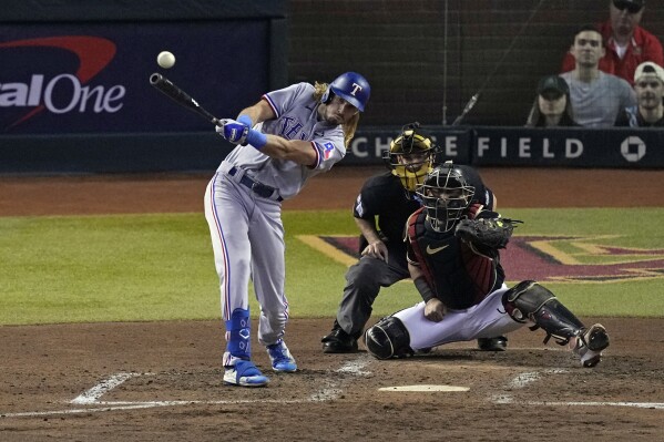 Texas Rangers' Travis Jankowski, left, hits a two-run double as Arizona Diamondbacks catcher Gabriel Moreno reaches for the pitch during the third inning in Game 4 of the baseball World Series Tuesday, Oct. 31, 2023, in Phoenix. (AP Photo/Ross D. Franklin)