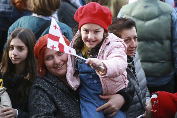 A woman holds her child waving a national flag as they celebrate Georgia's EU candidacy at Liberty Square in Tbilisi, Georgia, on Friday, Dec. 15, 2023. Several thousand people attend a march in support of Georgia's EU candidacy. European Union flags waved across Georgia Friday after the European Council took a step forward along the long road towards granting Georgia and Moldova as EU membership. (AP Photo/Zurab Tsertsvadze)