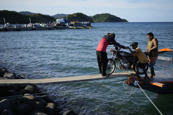 Workers push a motorcycle along a wooden plank at the port of the coastal town of Santa Ana, Cagayan province, northern Philippines on Tuesday, May 7, 2024. (AP Photo/Aaron Favila)