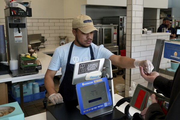 An employee collects payment at an Auntie Anne's and Cinnabon store in Livermore, Calif., Thursday, March 28, 2024. He's among hundreds of thousands of California fast-food workers who will be paid at least $20 an hour starting Monday, April 1. (AP Photo/Terry Chea)