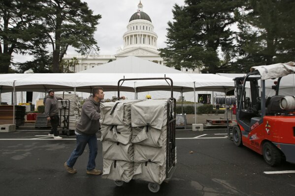 
              Jacob Blackwell moves a cart load of chairs in preparation for Monday's inauguration of Governor-elect Gavin Newsom, Saturday, Jan. 5, 2019, Sacramento, Calif. Due to the threat of rain, the inaugural ceremonies are expected to be held inside tents erected on the west side of the Capitol. (AP Photo/Rich Pedroncelli)
            