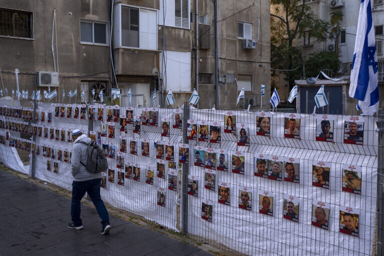A man passes by a fence with photographs of hostages, mostly Israeli civilians who were abducted during the Oct. 7, unprecedented Hamas attack on Israel, in Ramat Gan, Israel, Wednesday, Nov. 22, 2023. Israel and Hamas have reached an agreement for a four-day halt to the devastating war in Gaza, accompanied by the release of dozens of hostages held by the militant group in return for Palestinian prisoners jailed by Israel, mediators said Wednesday. (AP Photo/Oded Balilty)