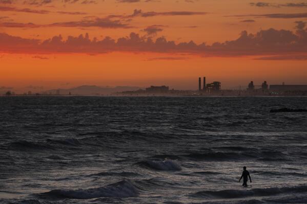 FILE - A man wades into the ocean at sunset, Tuesday, June 22, 2021, in Newport Beach, Calif. In a report released Wednesday, Dec. 8, 2021, the National Academy of Sciences says to fight climate change the world needs to look into the idea of making the oceans suck up more carbon dioxide. (AP Photo/Jae C. Hong, File)