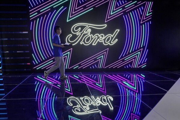 FILE - A worker walks past neon signs for Ford at the Auto Shanghai 2023 show in Shanghai, Tuesday, April 18, 2023. Ford reports their earnings on Wednesday, April 24, 2024. (AP Photo/Ng Han Guan, File)