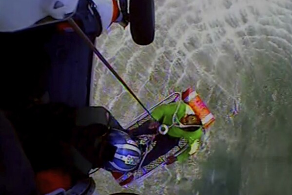 In this image taken from U.S. Coast Guard video, one of three fishermen is rescued from ocean waters by the Coast Guard five miles east of the island of Nantucket off the Cape Cod, Mass., coast Saturday, Aug. 5, 2023. The men were safely hoisted aboard the helicopter and flown to Hyannis Airport, where they were treated by emergency medical workers. (U.S Coast Guard via AP)