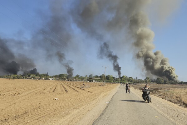Palestinians walk and drive away from Kibbutz Kfar Azza, Israel, near the fence with the Gaza strip following a deadly attack on the community on Saturday, Oct. 7, 2023. (AP Photo/Hassan Eslaiah)