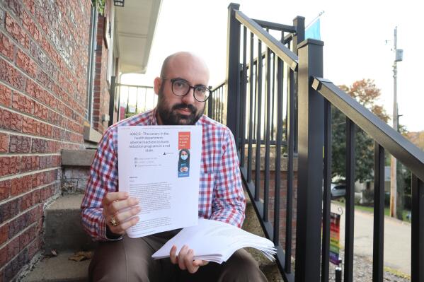 Dr. Frank Annie, a Republican city council candidate and research scientist specializing in cardiovascular health at Charleston Area Medical Center Memorial Hospital, holds up scientific papers he’s published on intravenous drug use in the city on the front steps of his home in Charleston, W.Va., Monday, Oct. 24, 2022. (AP Photo/Leah Willingham)