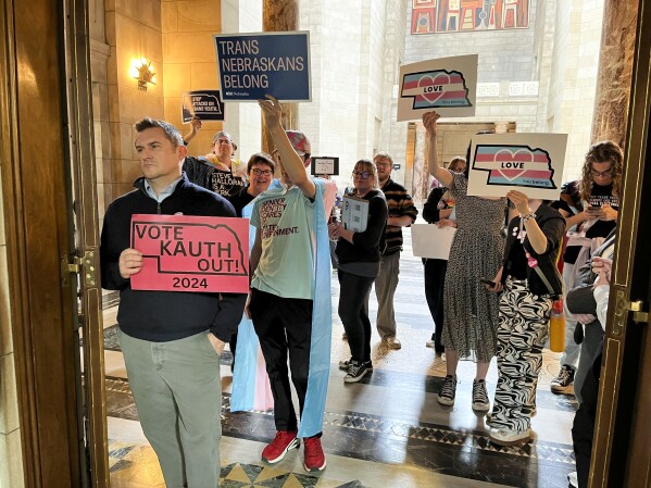 FILE - Protesters hold signs outside the doors of the legislative chamber in the Nebraska Capitol in response to a bill that would have restricted students to bathrooms, locker rooms and sports teams that correspond with the gender they were assigned at birth, April 5, 2024, in Lincoln, Neb. In a lawsuit filed Monday, April 29, four Republican state attorneys general are challenging a federal regulation that seeks to protect the rights of transgender students in the nation's schools by banning blanket policies that bar transgender students from school bathrooms aligning with their gender, among other provisions. (AP Photo/Margery Beck, File)