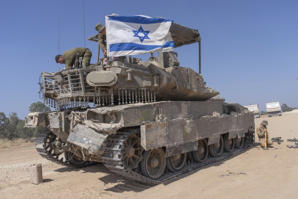 An Israeli soldier attaches an Israeli flag on top of an armoured personnel carriers (APC) near Israel's border with Gaza, in southern Israel, Monday, April 15, 2024. (AP Photo/Ohad Zwigenberg)