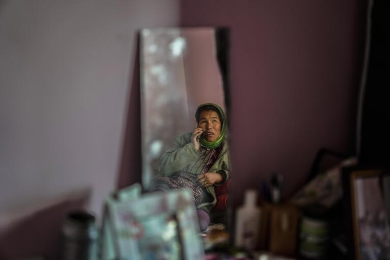 Sonam Kunkhen, Konchok Dorjey's wife is reflected in a mirror as she talks on cell phone inside her home in Kharnakling near Leh town in the cold desert region of Ladakh, India, Friday, Sept. 16, 2022. “It's better here for me and my family,” she said. “It took us a while to adjust, but I'm glad we moved here.” (AP Photo/Mukhtar Khan)