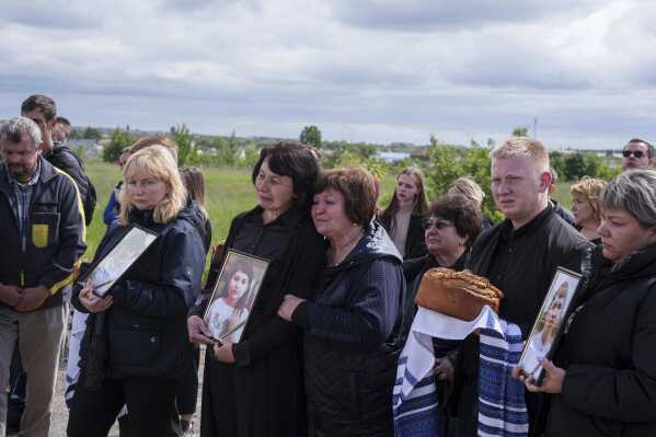 People hold photographs of Roman Martyniuk, 17, Tamara Martyniuk, 8, and Stanislav Martyniuk, 12, killed in a Russian strike on Sunday, during farewell ceremony in Korostyshiv, Zhytomyr region, Ukraine, Wednesday, May 28, 2025. (AP Photo/Evgeniy Maloletka)