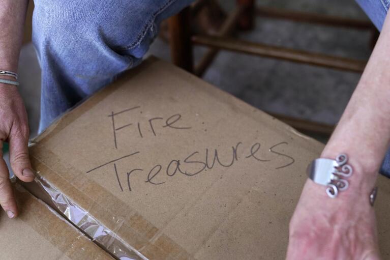 Ellie Holden prepares to open a box of "fire treasures", which are the burnt remains of their family's California home, Thursday, May 12, 2022, in Proctor, Vt. After fleeing one of the most destructive fires in California, the Holden family wanted to find a place that had not been so severely affected by climate change and chose Vermont. The few things the Holdens recovered are now boxed in the dairy barn — a burnt trombone, plant hanger, piano brackets, a jewelry box, a ladle, wedding silverware. (AP Photo/Charles Krupa)