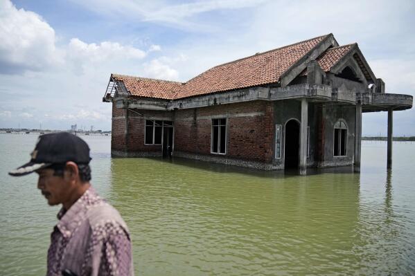 FILE - A man walks past a house abandoned after it was inundated by water due to the rising sea level in Sidogemah, Central Java, Indonesia, Nov. 8, 2021. Climate hazards such as flooding, heat waves and drought have worsened more than half of the hundreds of known infectious diseases in people, such as malaria, hantavirus, cholera and even anthrax, according to a new study released Monday, Aug. 8, 2022. (AP Photo/Dita Alangkara, File)