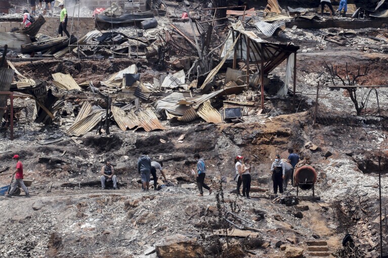 Locals clean the rubble of burnt-out houses after forest fires reached their neighborhood in Vina del Mar, Chile, Sunday, Feb. 4, 2024. (AP Photo/Cristobal Basaure)