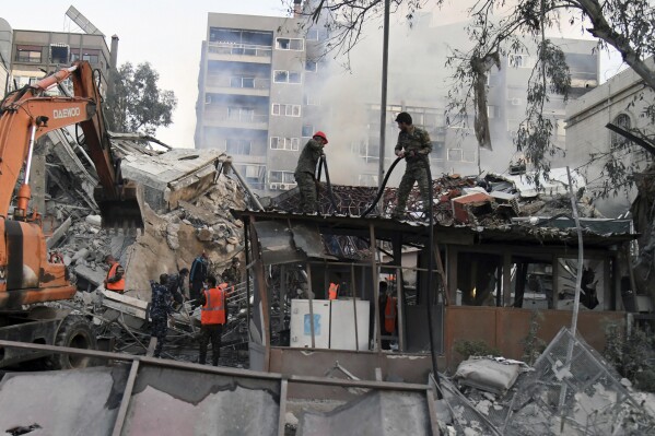 In this photo released by the official Syrian state news agency SANA, emergency service workers clear the rubble at a destroyed building struck by Israeli jets in Damascus, Syria, Monday, April 1, 2024. An Israeli airstrike has destroyed the consular section of Iran's embassy in Syria, killing a senior Iranian military adviser and roughly a handful of other people, Syrian state media said Monday. (SANA via AP)