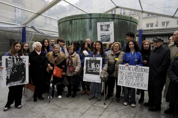 CAPTION CORRECTS NAME TO ESTHER SENOT French nazi hunter Serge Klarsfeld, right, his wife Beata, second from right, French Holocaust survivors, Esther Senot, third from left, and Ginette Kolinka, fifth from left, attend a gathering in the Paris Holocaust memorial to sound the alarm about resurgent antisemitic hate speech, graffiti and abuse linked to the Israel-Hamas war, in Paris, Saturday, Nov. 18, 2023. rance's Interior Ministry said this week that 1,762 antisemitic acts have been reported this year, as well as 131 anti-Muslim acts and 564 anti-Christian acts. The placard on the right reads "we won't let history repeat itself, or stutter". (AP Photo/Thibault Camus)