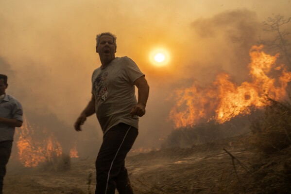 A local reacts as the flames burn trees in Gennadi village, on the Aegean Sea island of Rhodes, southeastern Greece, on Tuesday, July 25, 2023. A firefighting plane has crashed in southern Greece, killing both crew members, as authorities are battling fires across the country amid a return of heat wave temperatures. (AP Photo/Petros Giannakouris)